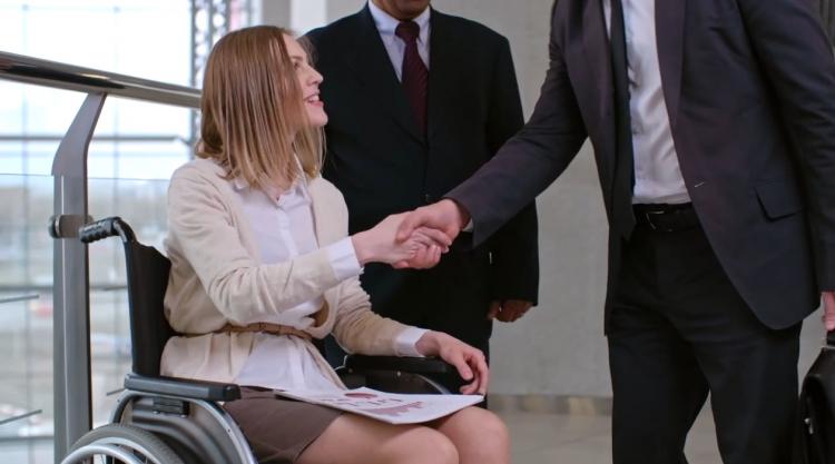 Professional woman in wheelchair shaking hands with a man in a dark suit.